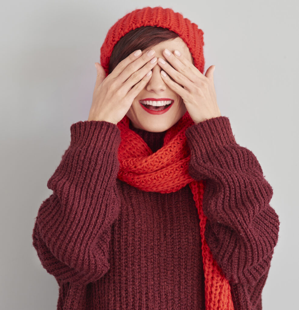Na obrázku je mladá žena, která si zakrývá hravě oči rukama. Je od pohledu veselá – široce se usmívá. Má zřejmě ráda červenou barvu, protože má svetr, šálu, čepici i rtěnku v odstínech červené.